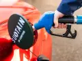 Tankowanie czerwonego samochodu paliwami syntetycznymi. Dystrybutor z niebieską rękojeścią w dłoni.