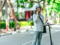 Młody mężczyzna w kasku rozmawia przez telefon, stojąc obok hulajnogi elektrycznej. Czy na hulajnodze elektrycznej trzeba mieć kask? On ma, więc chyba tak!