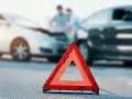 Trójkąt ostrzegawczy na drodze po wypadku. Dwa uszkodzone samochody i dwie osoby rozmawiające. Ważne, by mieć odpowiednią suma gwarancyjna OC.