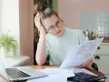 Zmartwiona kobieta analizuje dokumenty, szukając informacji o zwrocie OC po sprzedaży samochodu. Obok laptop i kalkulator.