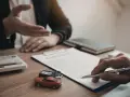 Rozmowa o zmianie ubezpieczyciela OC. Na stole leży umowa, kluczyki do auta i zabawkowy samochód.