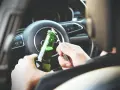 Ręce otwierają butelkę piwa za kierownicą. To niebezpieczna jazda pod wpływem alkoholu, która może skończyć się tragicznie.
