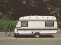 Biała przyczepa kempingowa "Classic" z czarnymi pasami i ozdobnymi ptakami na dachu. Idealna kategoria na auto dla podróżujących.