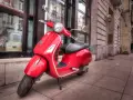 Czerwony skuter Vespa na chodniku. Zastanawiasz się, od ilu lat można jeździć motorowerem?