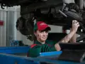Mechaniczka z plamami smaru na twarzy pracuje pod samochodem, oferując fachową assistance midi.