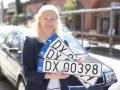 Kobieta trzyma tablice rejestracyjne z oznaczeniem DX. Nowa rejestracja samochodu w Polsce.