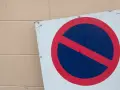 Znak zakaz postoju na białym tle, z czerwonym okręgiem i przekreśleniem na niebieskim tle.
