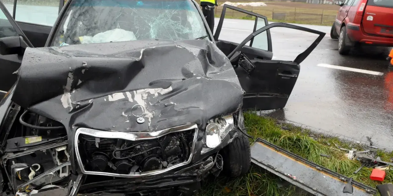 Zniszczony czarny samochód po wypadku, z otwartymi drzwiami i poobijanym przodem. Policjant stoi obok. Zastanawiasz się, ile wzrasta OC po szkodzie?