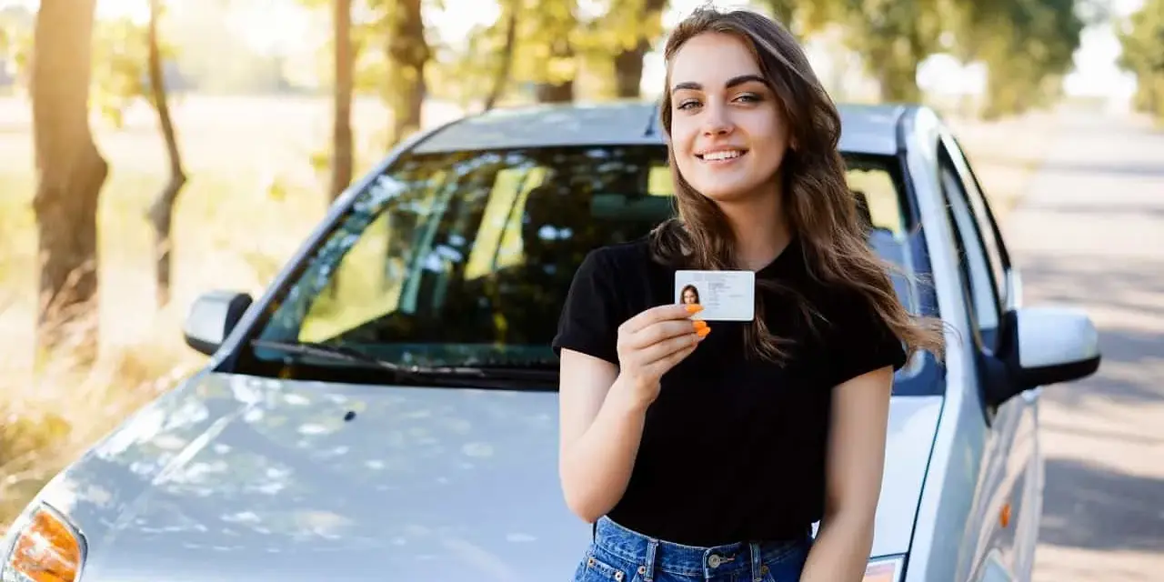 Szczęśliwa młoda kobieta z prawem jazdy 16 lat stoi obok samochodu.
