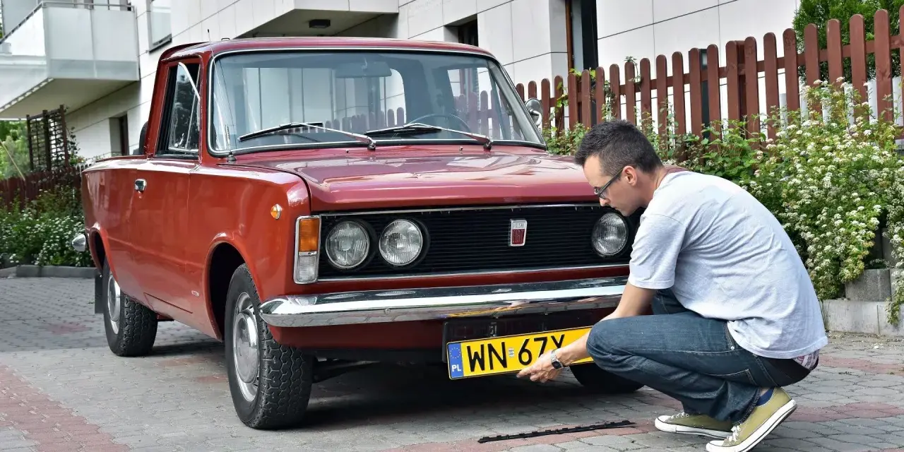 Mężczyzna montuje tablicę rejestracyjną do zabytkowego Fiata 125p. Proces ten jest kluczowy, by móc zarejestrować auto na zabytek.