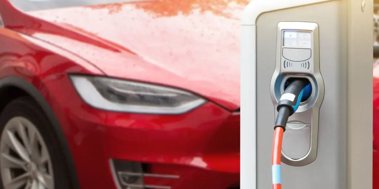 Czerwona Tesla podłączona do ładowarki. Zastanawiasz się, ile ładuje się Tesla? Czas ładowania zależy od modelu i mocy ładowarki.