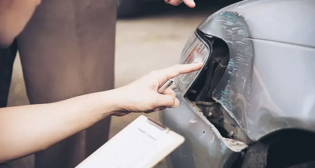 Dwóch mężczyzn ocenia szkody parkingowe na samochodzie. Jeden wskazuje palcem na uszkodzony reflektor, drugi trzyma dokumenty.