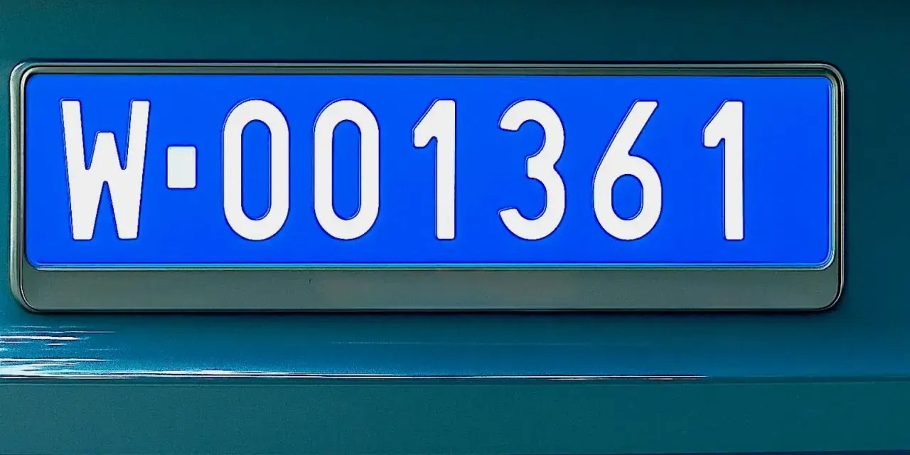 Niebieskie tablice rejestracyjne z numerem W-001361 na ciemnozielonym samochodzie.