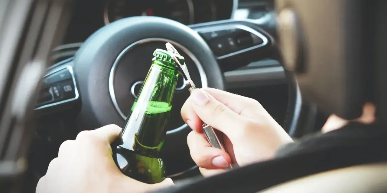 Ręce otwierają butelkę piwa za kierownicą. To niebezpieczna jazda pod wpływem alkoholu, która może skończyć się tragicznie.