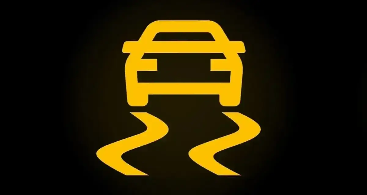 Żółty symbol ESP na czarnym tle. Auto jedzie po śliskiej drodze, co oznacza, że system kontroli trakcji jest aktywny.