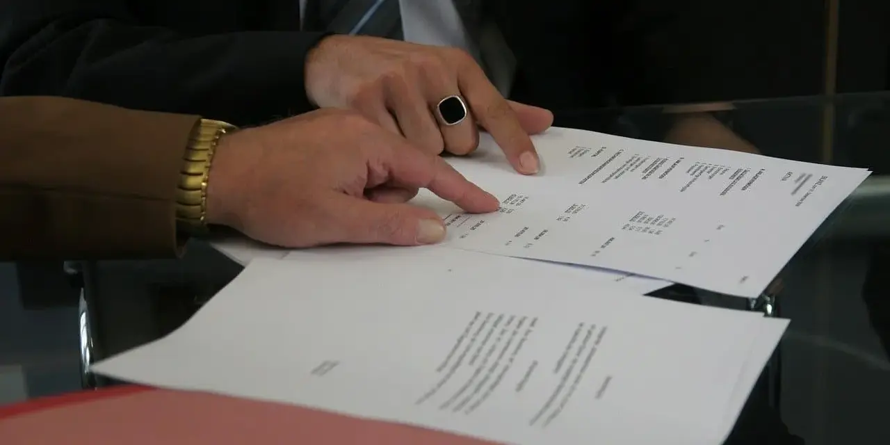 Dwóch mężczyzn analizuje dokumenty, jeden wskazuje palcem na tekst. Może to być wypowiedzenie umowy AC.