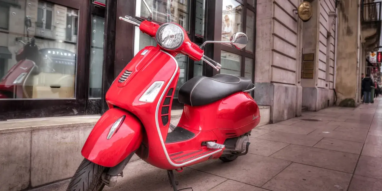 Czerwony skuter Vespa na chodniku. Zastanawiasz się, od ilu lat można jeździć motorowerem?