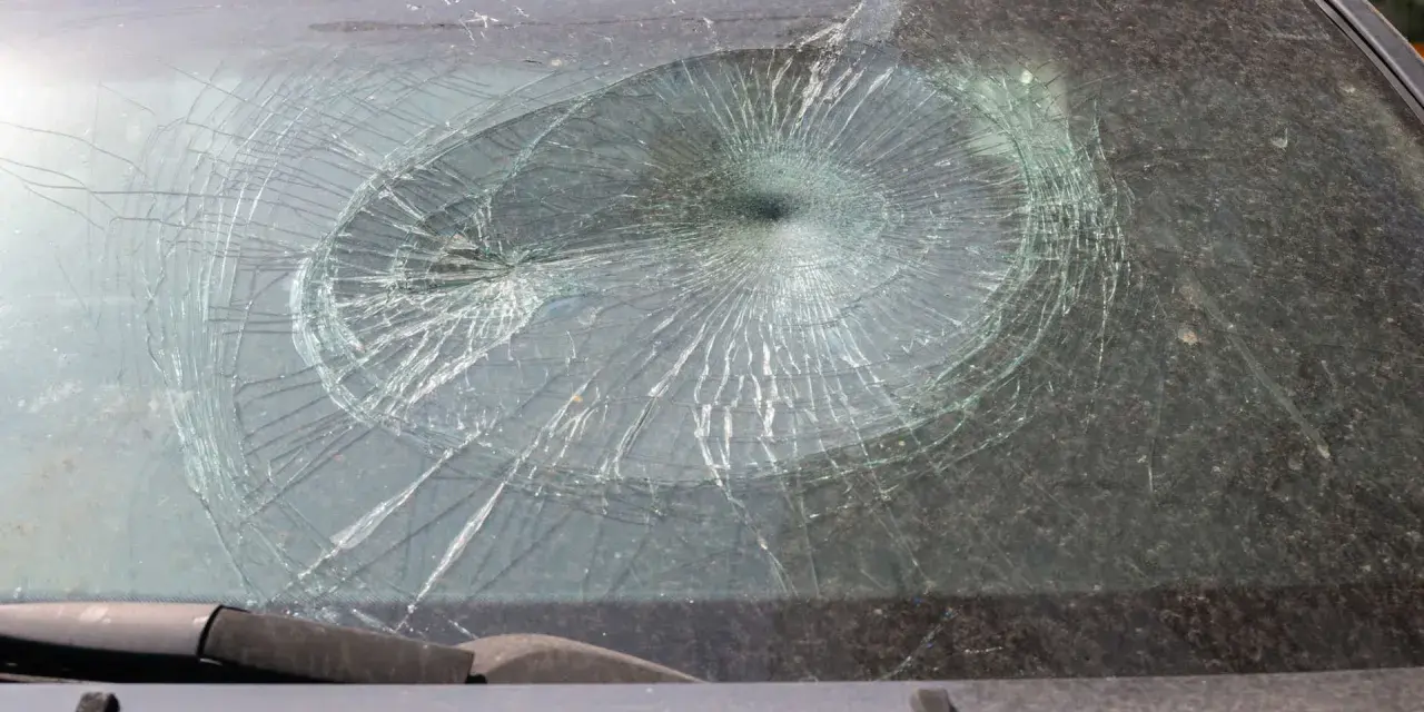 Pęknięta szyba w aucie, z pajęczyną pęknięć rozchodzących się od centralnego punktu.