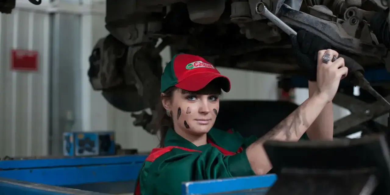 Mechaniczka z plamami smaru na twarzy pracuje pod samochodem, oferując fachową assistance midi.
