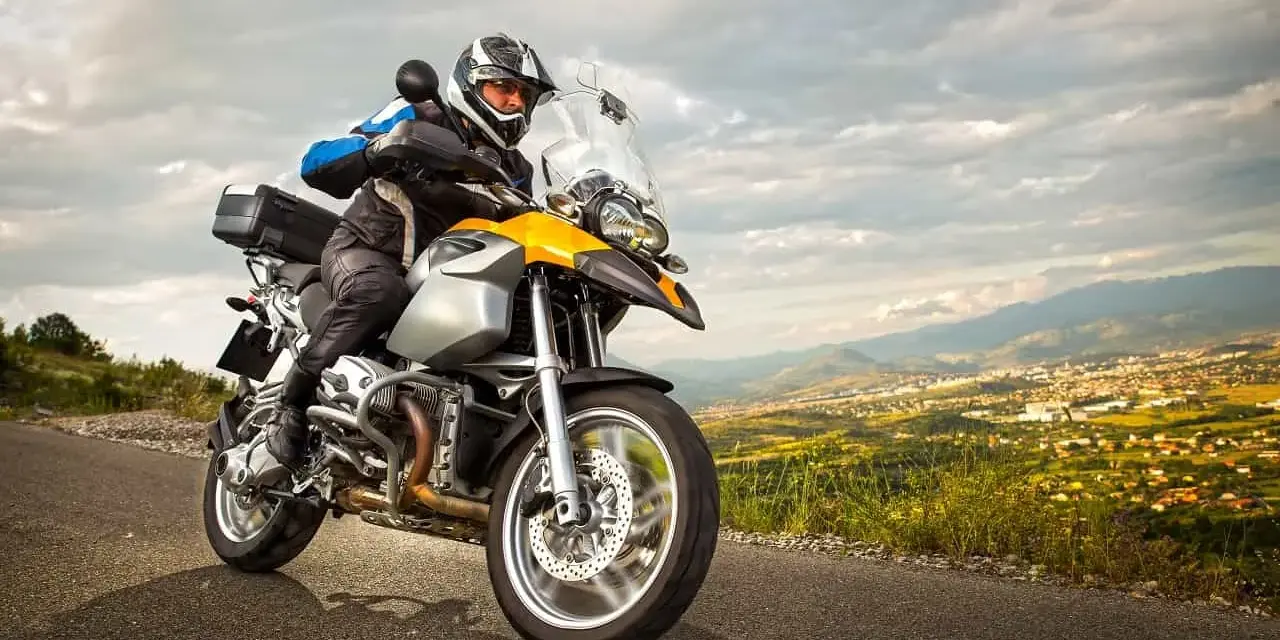 Motocyklista w kasku i kurtce jedzie drogą z widokiem na miasto w oddali. To może być początek jego przygody z rejestracją motocykla z zagranicy.