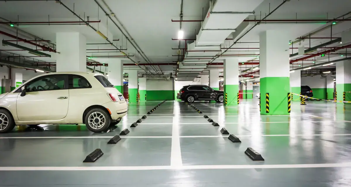 Jasny samochód i ciemny SUV na parkingu podziemnym. Widać odległość miejsca postojowego od ściany, zaznaczoną przez czarne odbojniki.