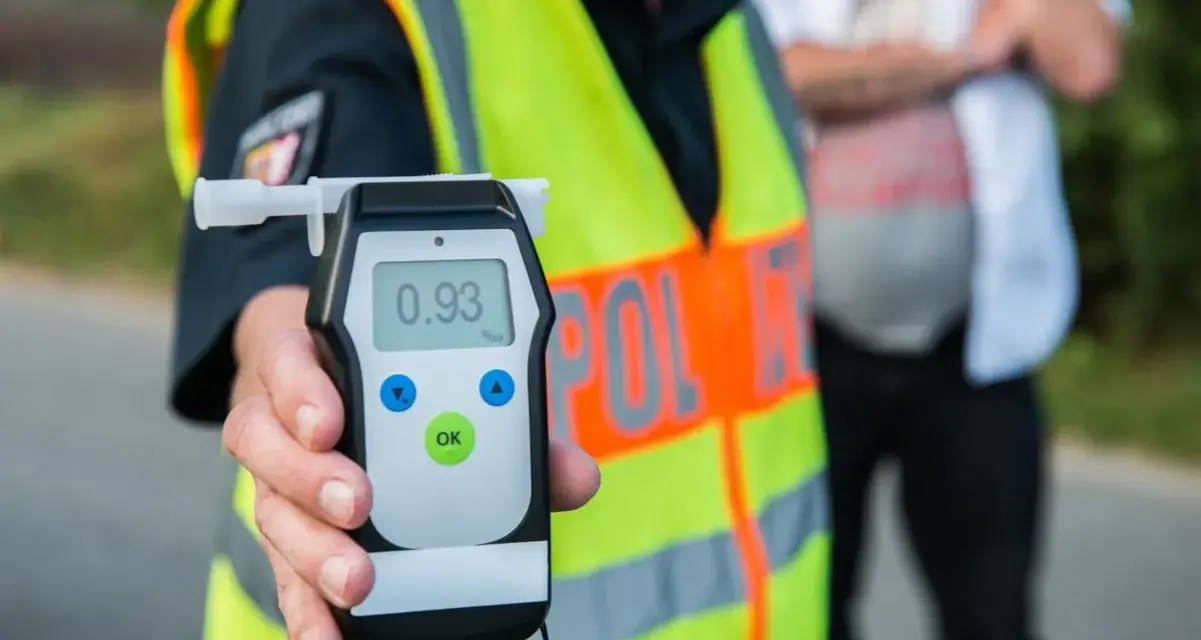Policjant w kamizelce odblaskowej pokazuje alkomat z wynikiem 0.93 promila. Rutynowa kontrola trzeźwości na drodze.