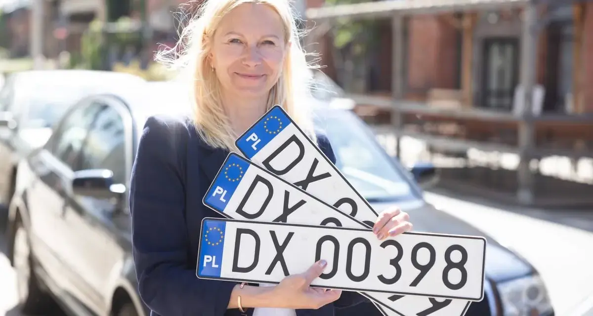 Kobieta trzyma tablice rejestracyjne z oznaczeniem DX. Nowa rejestracja samochodu w Polsce.