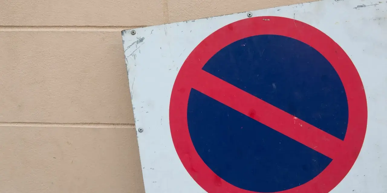 Znak zakaz postoju na białym tle, z czerwonym okręgiem i przekreśleniem na niebieskim tle.