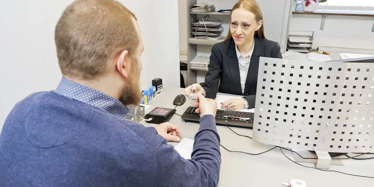 Mężczyzna przekazuje dokument urzędniczce, kiedy wymiana prawa jazdy jest w toku.