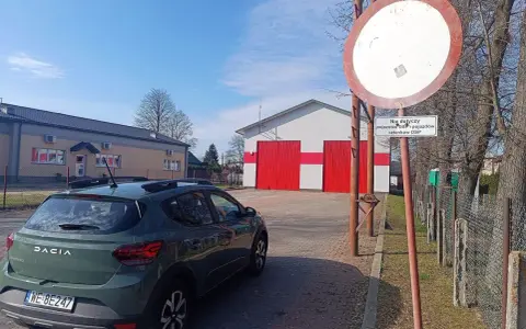 Zielony Dacia Sandero zaparkowany przy remizie OSP. Znak zakazu wjazdu, który może oznaczać mandat za wjazd pod zakaz, jest widoczny obok.