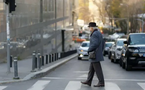Starszy pan w kapeluszu i maseczce przechodzi przez pasy, unikając potrącenia na ruchliwej ulicy.