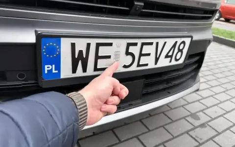Palec wskazuje hologram na tablicy rejestracyjnej. Uniknij kary za nieprzerejestrowanie pojazdu, dbając o aktualność dokumentów.