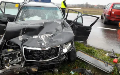 Zniszczony czarny samochód po wypadku, z otwartymi drzwiami i poobijanym przodem. Policjant stoi obok. Zastanawiasz się, ile wzrasta OC po szkodzie?