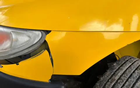 Uszkodzony żółty zderzak i błotnik, widoczna lampa. Potrzebna wycena naprawy samochodu wzór.