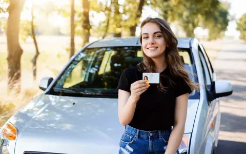 Szczęśliwa młoda kobieta z prawem jazdy 16 lat stoi obok samochodu.