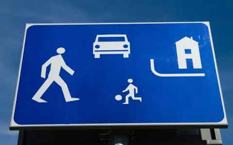 Znak strefa zamieszkania: pieszy, samochód, dziecko grające w piłkę i dom. Bezpieczna przestrzeń dla wszystkich.