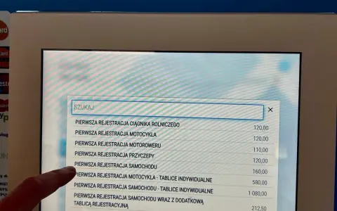 Palec wskazuje opcję "PIERWSZA REJESTRACJA SAMOCHODU" na ekranie, gdzie szukamy informacji, jak napisać upoważnienie do wyrejestrowania samochodu.
