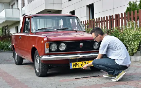 Mężczyzna montuje tablicę rejestracyjną do zabytkowego Fiata 125p. Proces ten jest kluczowy, by móc zarejestrować auto na zabytek.