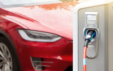 Czerwona Tesla podłączona do ładowarki. Zastanawiasz się, ile ładuje się Tesla? Czas ładowania zależy od modelu i mocy ładowarki.