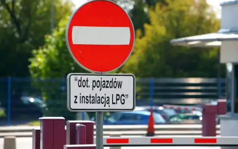 Zakaz wjazdu znak dla pojazdów z instalacją LPG. Barierka i budynek w tle.