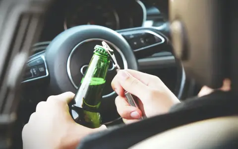 Ręce otwierają butelkę piwa za kierownicą. To niebezpieczna jazda pod wpływem alkoholu, która może skończyć się tragicznie.