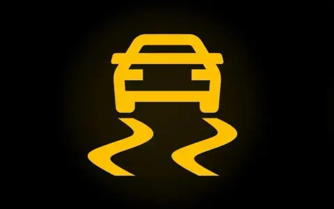 Żółty symbol ESP na czarnym tle. Auto jedzie po śliskiej drodze, co oznacza, że system kontroli trakcji jest aktywny.