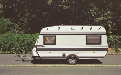 Biała przyczepa kempingowa "Classic" z czarnymi pasami i ozdobnymi ptakami na dachu. Idealna kategoria na auto dla podróżujących.