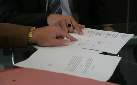 Dwóch mężczyzn analizuje dokumenty, jeden wskazuje palcem na tekst. Może to być wypowiedzenie umowy AC.