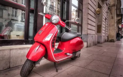 Czerwony skuter Vespa na chodniku. Zastanawiasz się, od ilu lat można jeździć motorowerem?