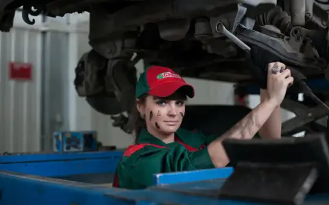 Mechaniczka z plamami smaru na twarzy pracuje pod samochodem, oferując fachową assistance midi.
