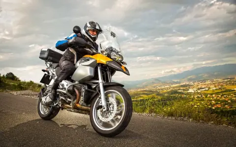 Motocyklista w kasku i kurtce jedzie drogą z widokiem na miasto w oddali. To może być początek jego przygody z rejestracją motocykla z zagranicy.