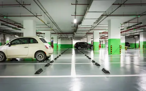 Jasny samochód i ciemny SUV na parkingu podziemnym. Widać odległość miejsca postojowego od ściany, zaznaczoną przez czarne odbojniki.