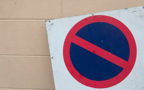 Znak zakaz postoju na białym tle, z czerwonym okręgiem i przekreśleniem na niebieskim tle.