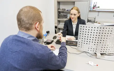 Mężczyzna przekazuje dokument urzędniczce, kiedy wymiana prawa jazdy jest w toku.